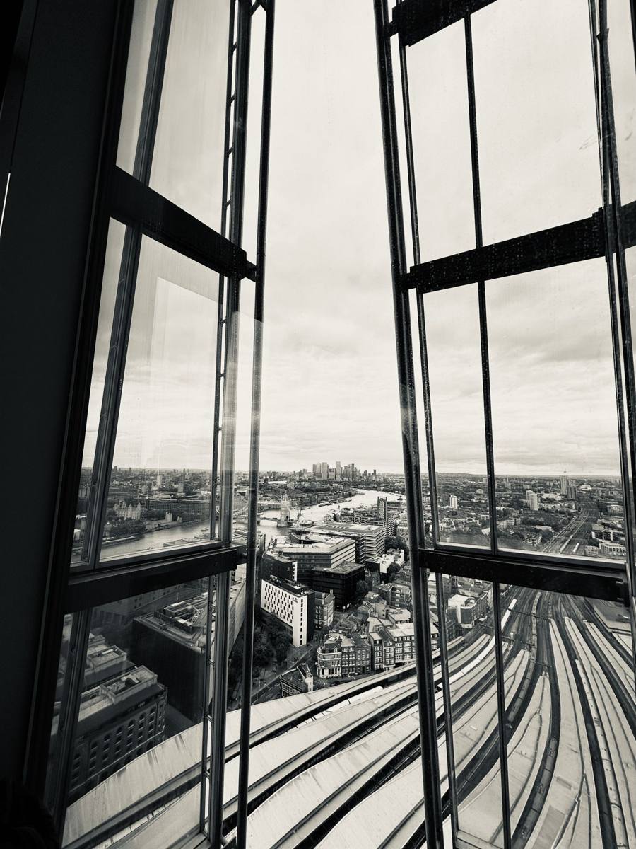 Black-and-white view through tall window frames over London rail lines and rooftops