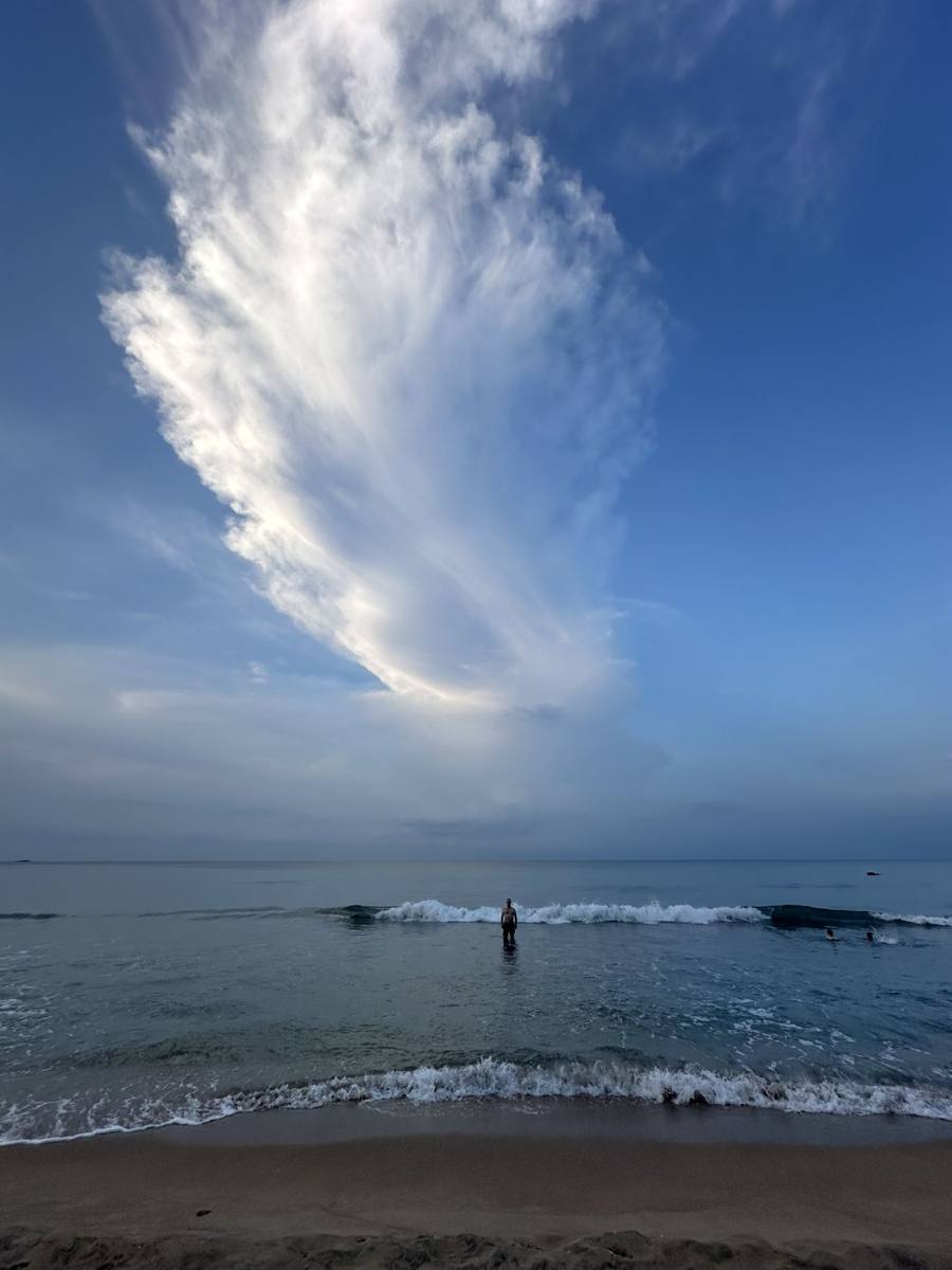 Plume of cloud over the sea, a lone figure in the surf